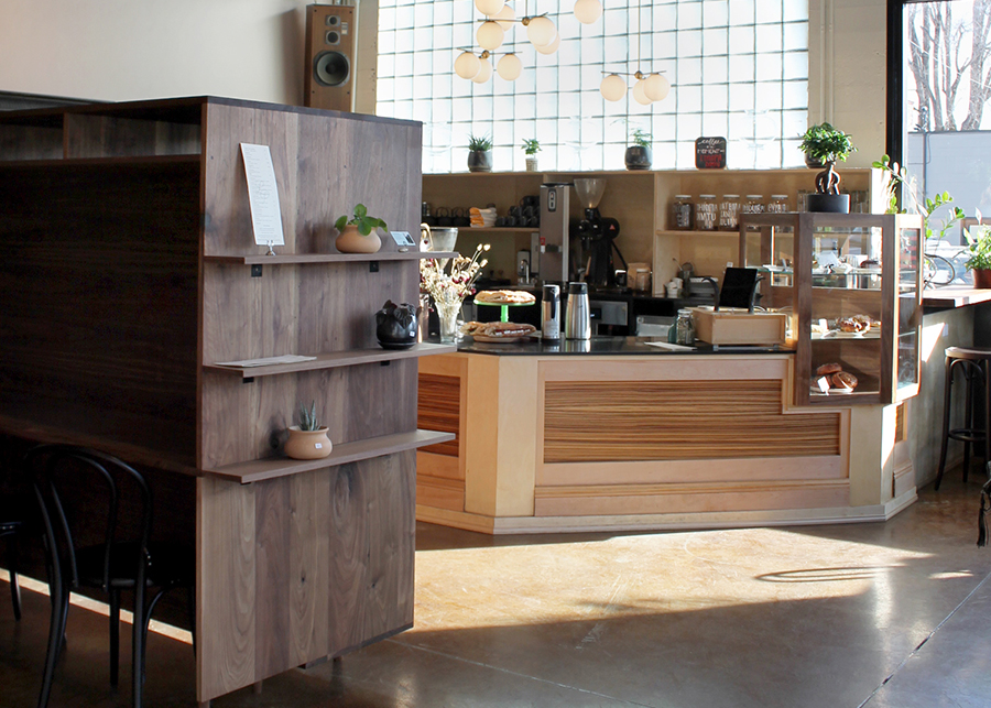 The custom counter front made from various types of wood can be seen behind a minimalist retail display case of dark-stained wood